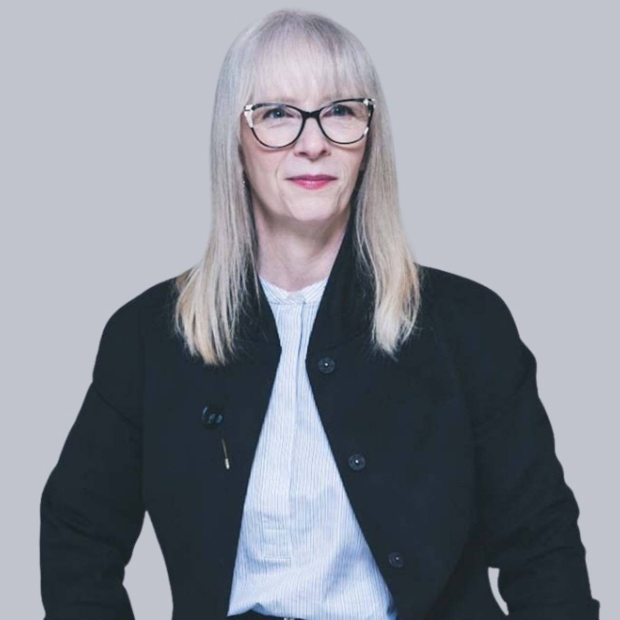 Ellen Finlay is a white woman with shoulder length blond hair wearing glasses, a black jacket and white blouse